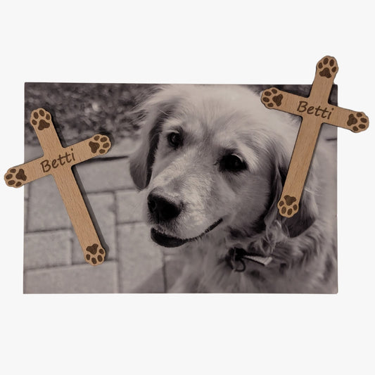 Schwarz-Weiß-Foto eines Hundes mit zwei Holzkreuzen als Magnete. Die Kreuze sind mit kleinen Pfotenabdrücken verziert und tragen den Namen „Betti“.